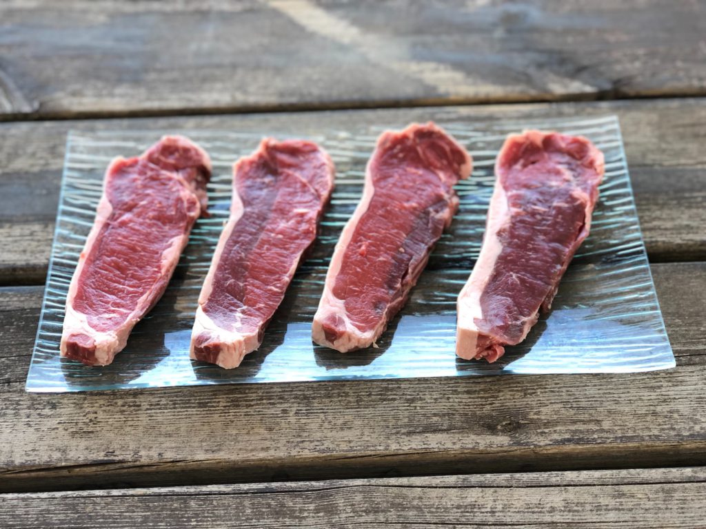 4 strip steaks on a wooden plank background