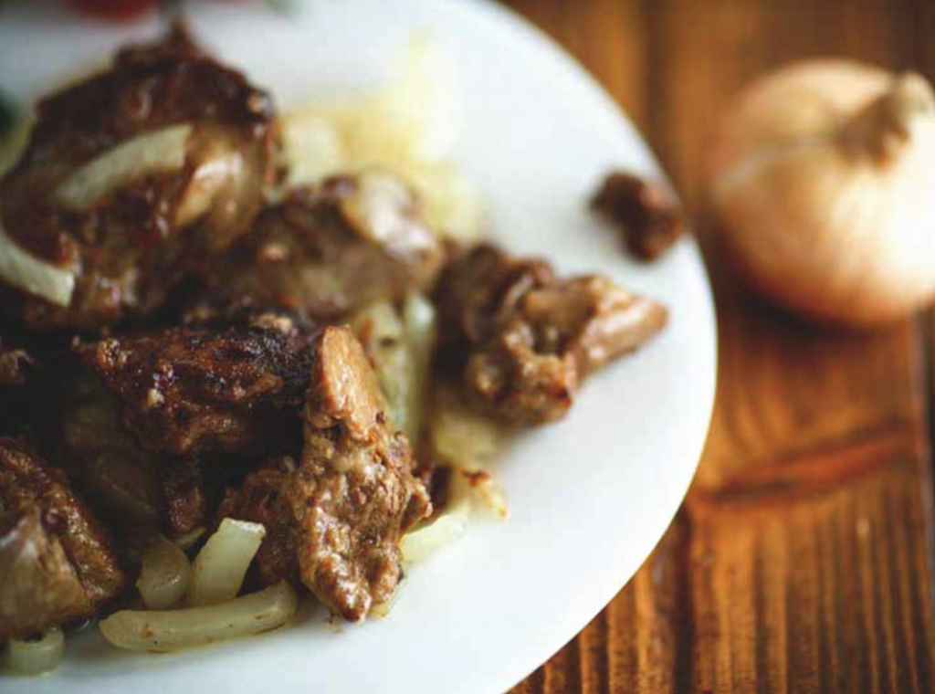 plate of cooked liver and onions on a wood table