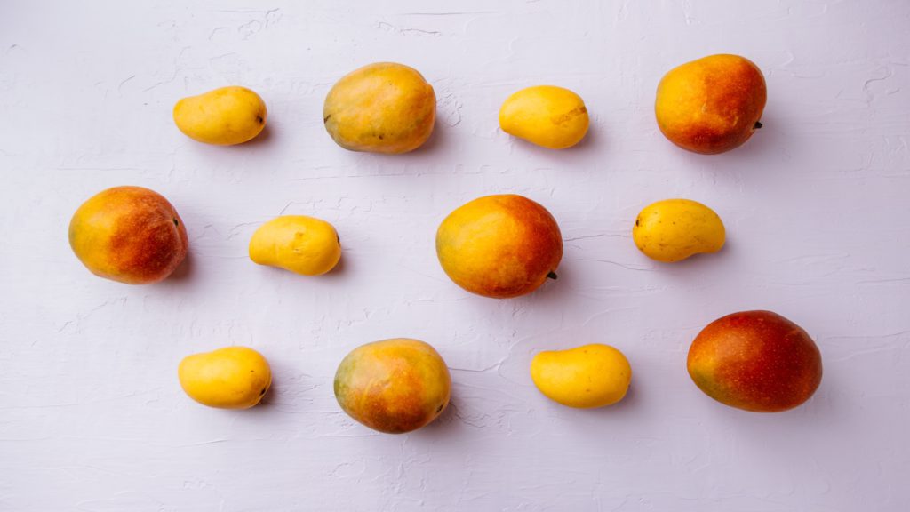 assorted sizes of mangoes on a white surface