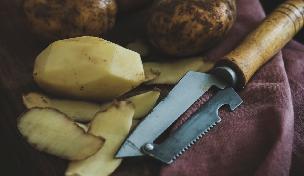 Peeled russet potato next to a peeler