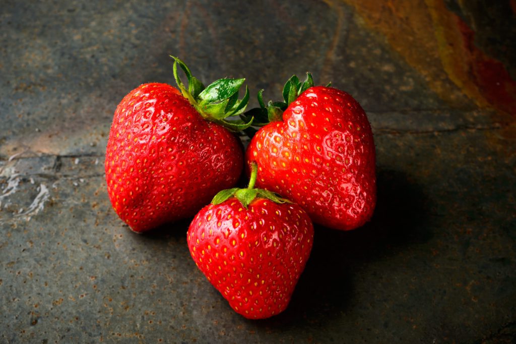 3 strawberries on a stone surface