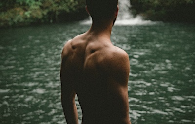 Shirtless man standing near waterfall