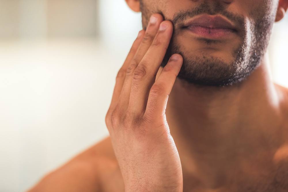 Man with short stubble touching his face